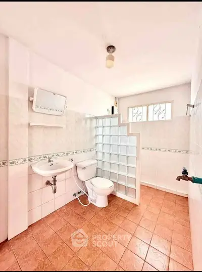 Spacious bathroom with modern glass block partition and tiled flooring.