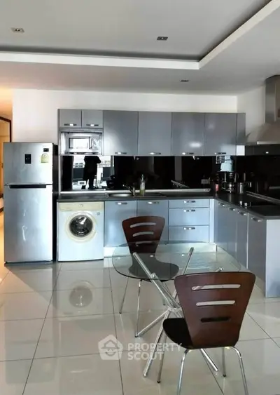 Modern kitchen with sleek cabinets, washing machine, and dining area in open layout.