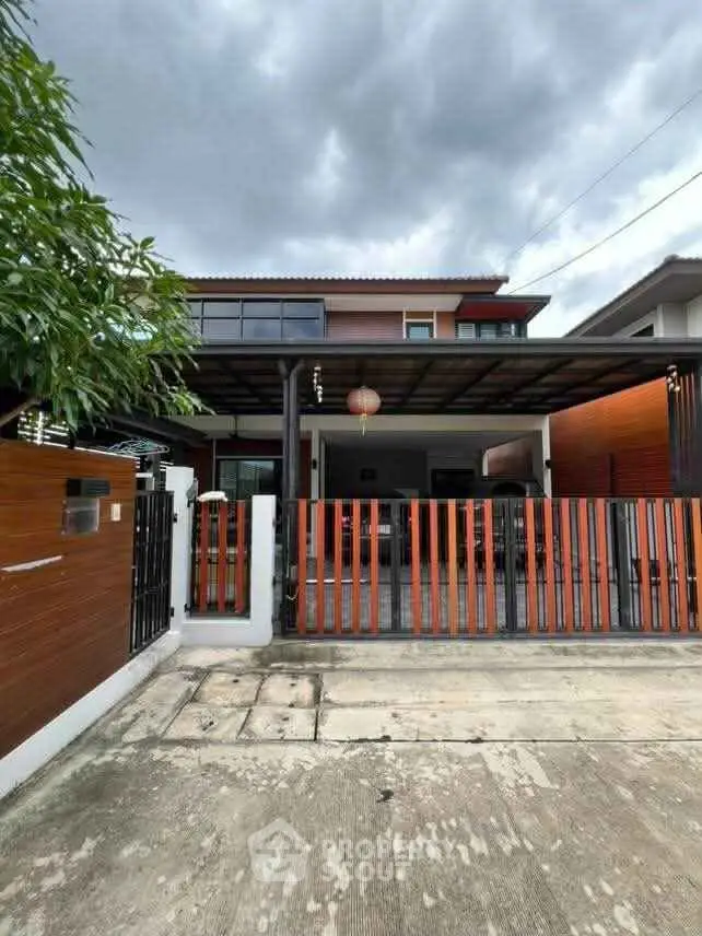 Modern two-story house with spacious driveway and stylish wooden gate under cloudy sky.