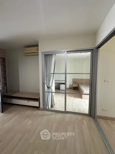 Spacious apartment with sliding glass doors and wooden flooring, featuring a cozy bedroom view.