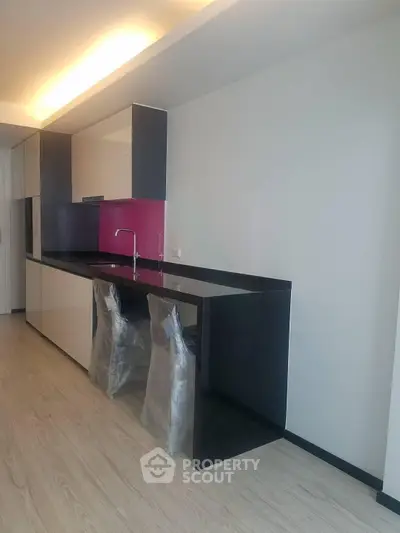 Modern kitchen with sleek black countertops and vibrant pink backsplash in a contemporary apartment.