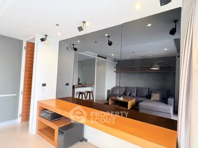 Modern living room with sleek design and large mirror wall, featuring cozy seating and stylish lighting.