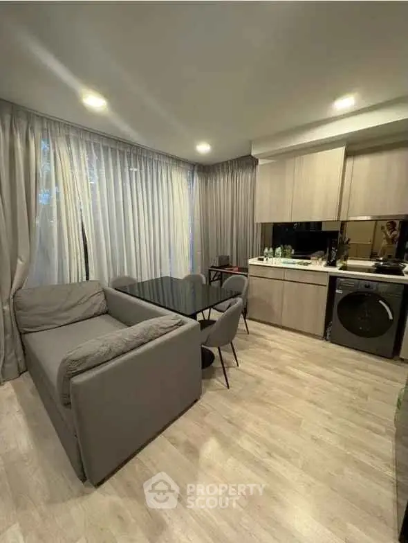 Modern open-layout living room with kitchen, featuring sleek furniture and natural light.