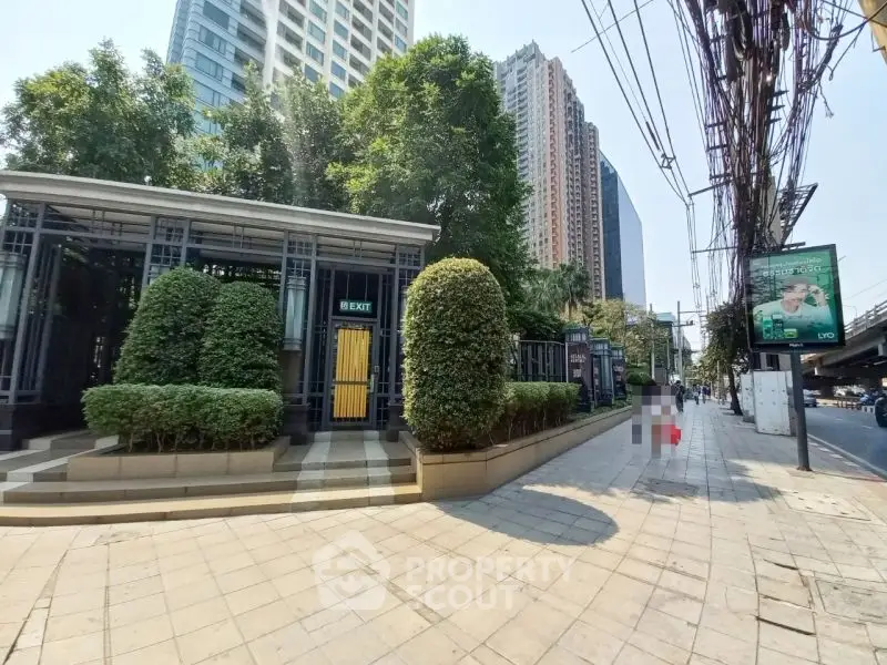 Modern urban building entrance with lush greenery and high-rise backdrop