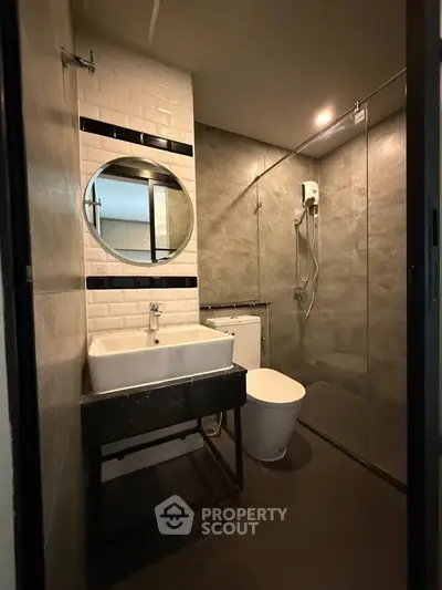 Modern bathroom with sleek design, featuring a round mirror, glass shower, and stylish sink.