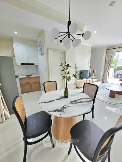 Modern dining area with marble table and stylish chandelier in open-plan living space.