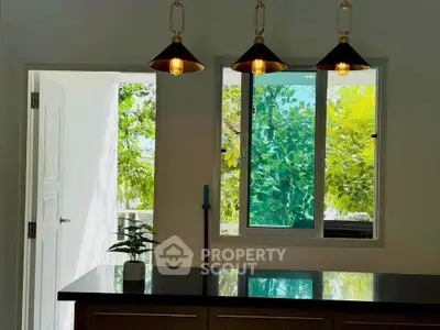 Modern kitchen with stylish pendant lights and lush green view.