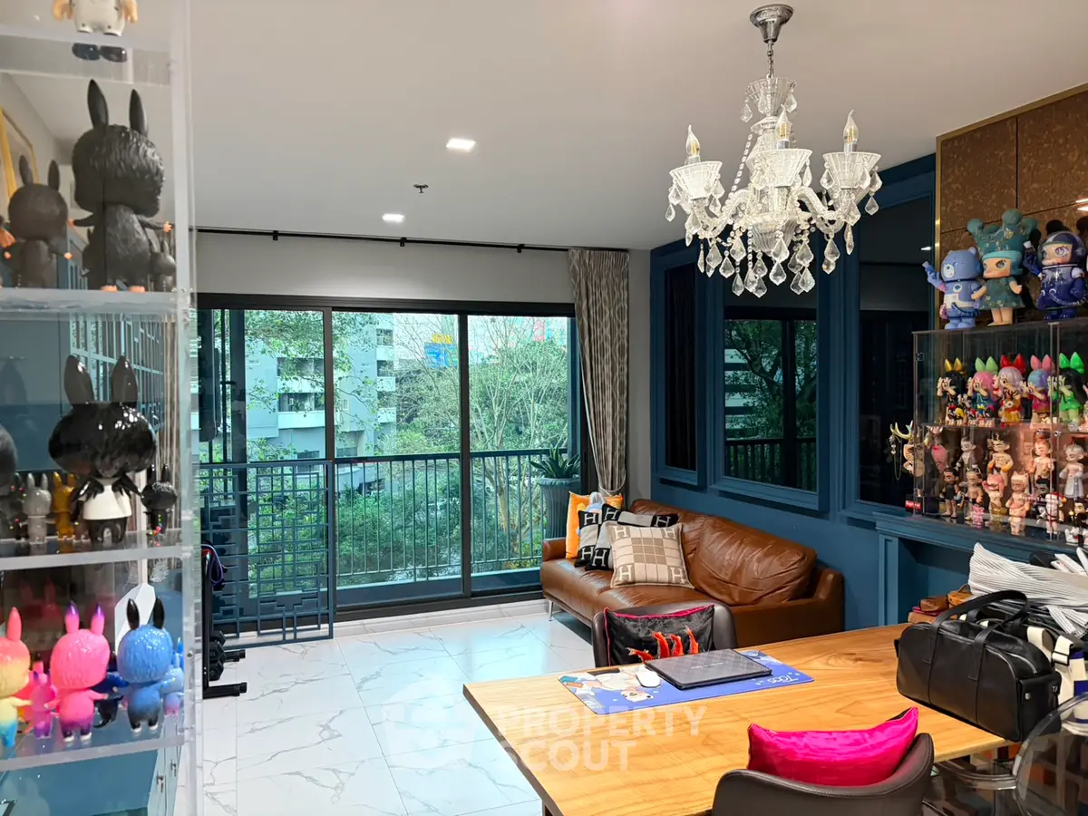Stylish living room with modern decor and large windows overlooking greenery, featuring a cozy leather sofa and elegant chandelier.