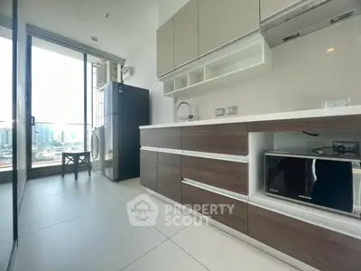 Modern kitchen with sleek cabinetry, large windows, and city view, featuring fridge, microwave, and washing machine.