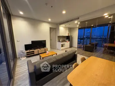Modern living room with open kitchen and city view, featuring sleek furniture and ambient lighting.