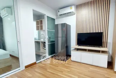 Modern living room with sleek design, featuring a TV, fridge, and air conditioning, adjacent to a compact kitchen.
