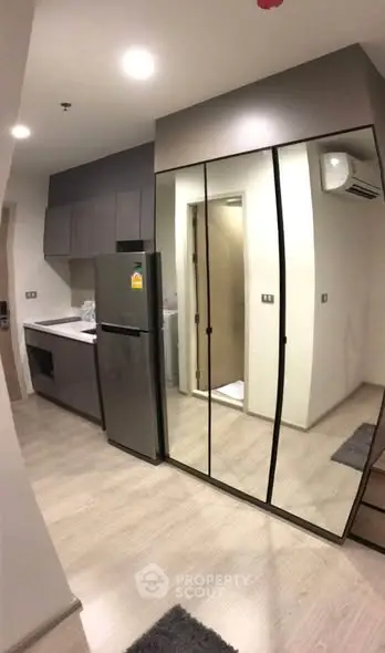 Modern compact kitchen with mirrored cabinets and sleek appliances in a stylish apartment.
