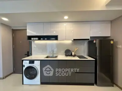 Modern kitchen with sleek cabinets, washing machine, and fridge in a stylish apartment.
