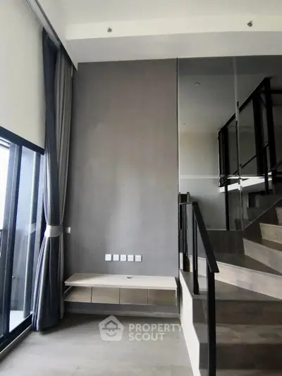 Modern duplex interior with high ceilings and large windows, featuring a sleek staircase and minimalist design.