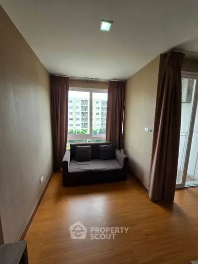 Cozy living room with wooden flooring and large window offering natural light and city view.
