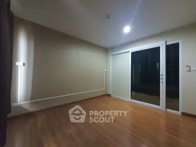 Spacious empty room with wooden flooring and large sliding glass door.