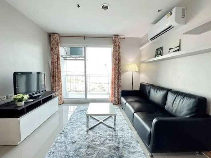 Modern living room with sleek black sofa, TV, and balcony view in a stylish apartment.