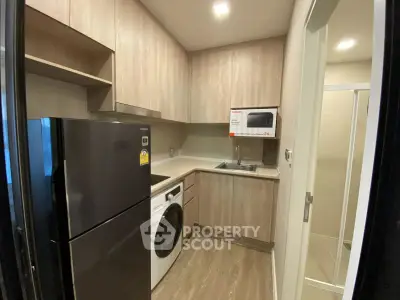 Modern kitchen with sleek appliances and wood cabinetry, featuring a washing machine and microwave.