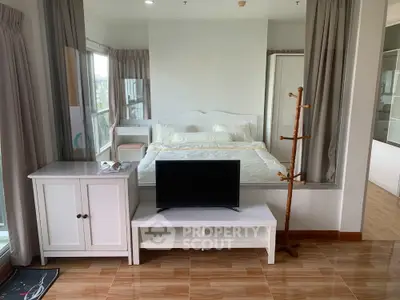 Modern bedroom with cozy bed, TV stand, and large windows offering natural light and city views.