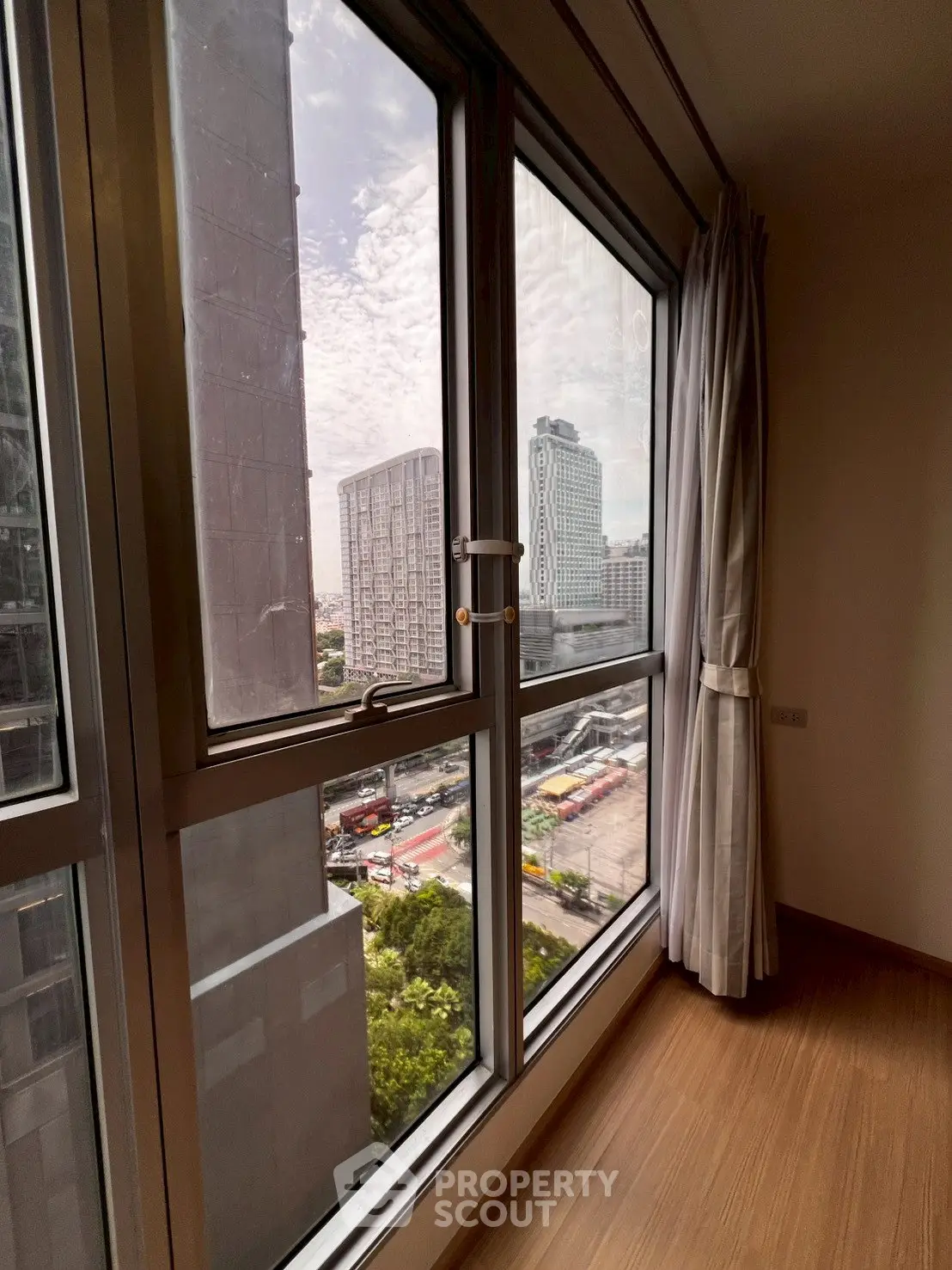 Stunning city view from modern apartment window with floor-to-ceiling glass and elegant curtains.