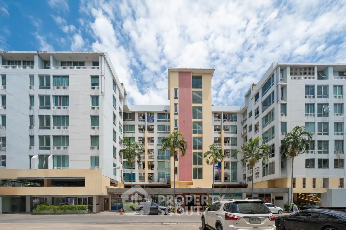 Modern apartment building with palm trees and parking area under a vibrant blue sky.