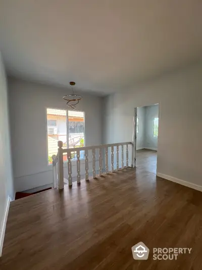 Spacious and well-lit upper-level living area with polished hardwood floors, elegant white balustrade, and a classic chandelier, offering a blank canvas for personalized interior design.