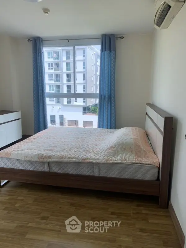 Spacious bedroom with large window and modern furnishings in a high-rise building.