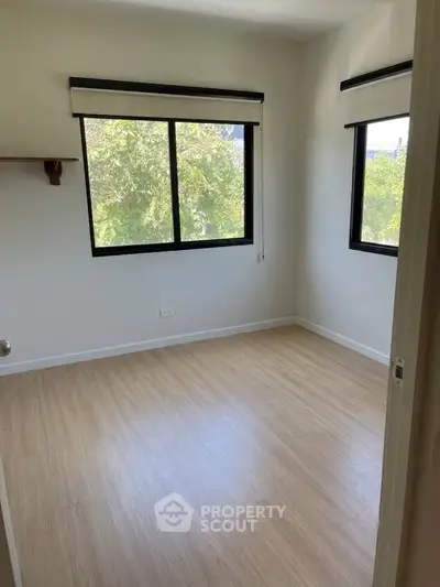 Bright empty bedroom with large windows and wooden flooring, perfect for customization.