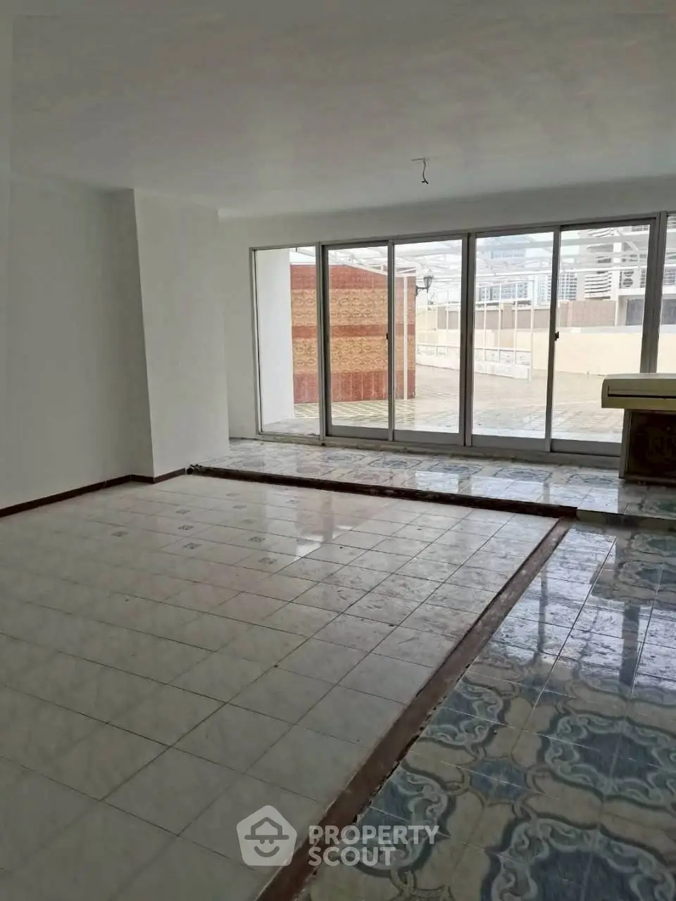 Spacious living room with large windows and tiled flooring, offering ample natural light and outdoor access.