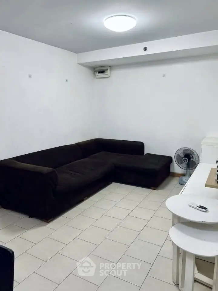 Spacious living room with dark sectional sofa and tiled flooring, ideal for cozy family gatherings.