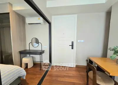 Modern bedroom with stylish furniture and wooden flooring, featuring a cozy workspace and air conditioning.