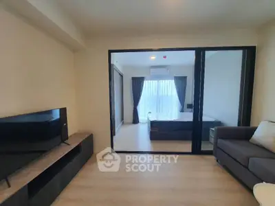 Modern living room with TV and view into a stylish bedroom through glass doors.