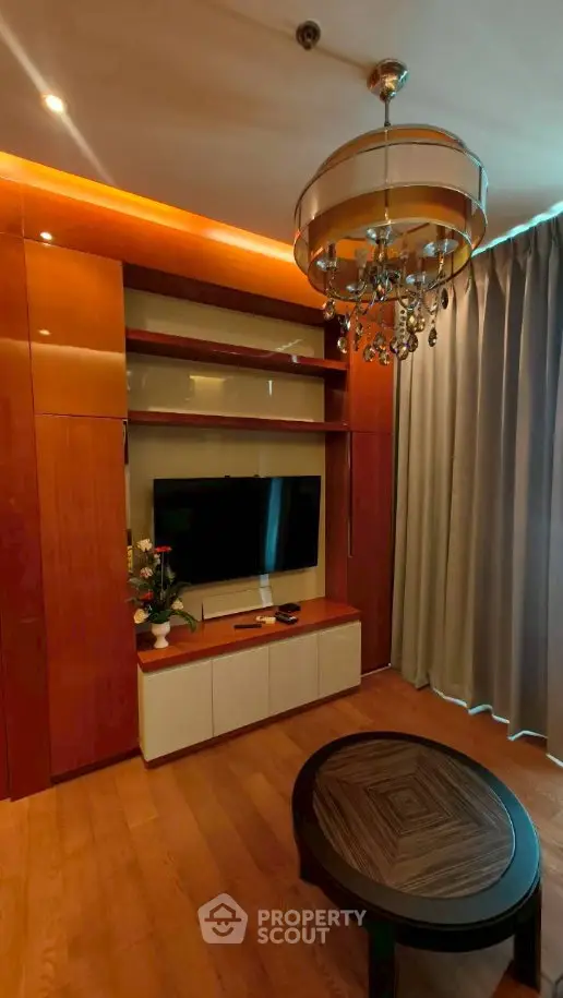 Elegant living room with modern chandelier and built-in TV unit, featuring warm wood tones and stylish decor.