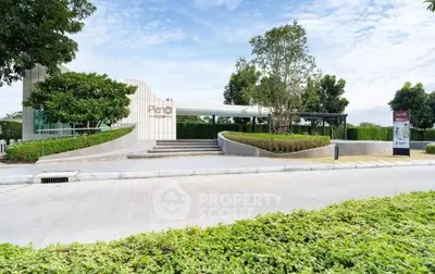 Modern building entrance with lush landscaping and clear blue sky, showcasing contemporary architecture.