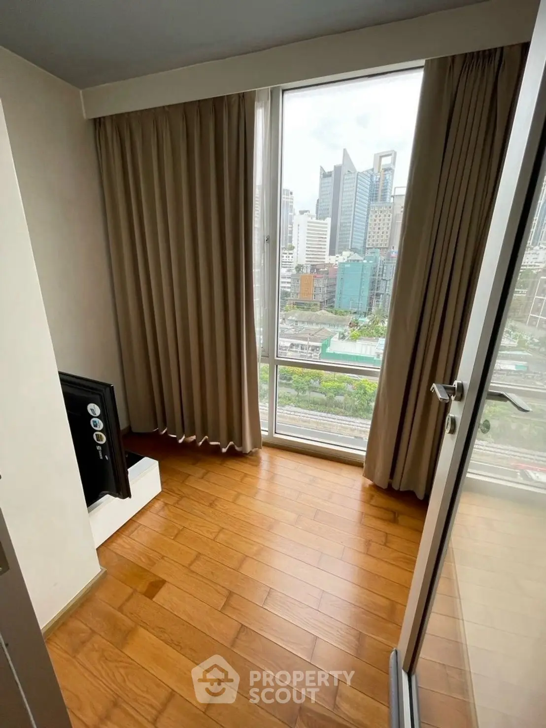 Cozy room with wooden flooring and city view through large window.