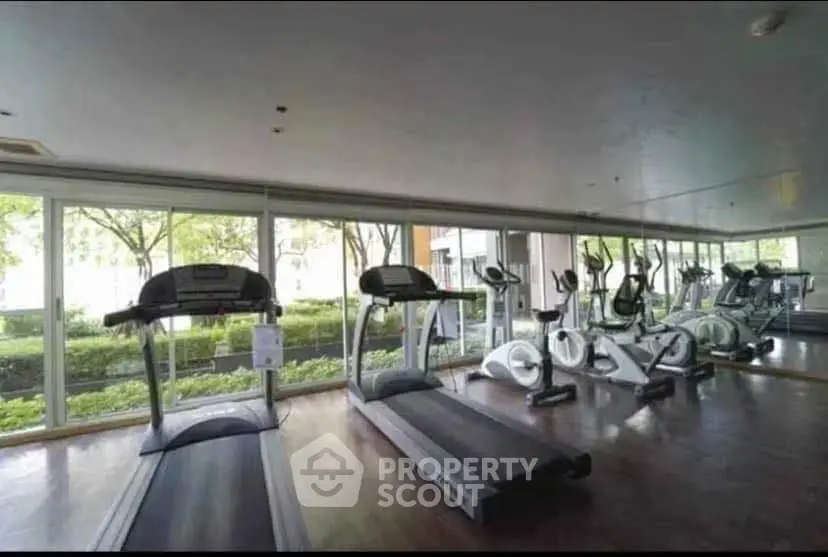 Spacious gym with modern equipment and large windows overlooking greenery.