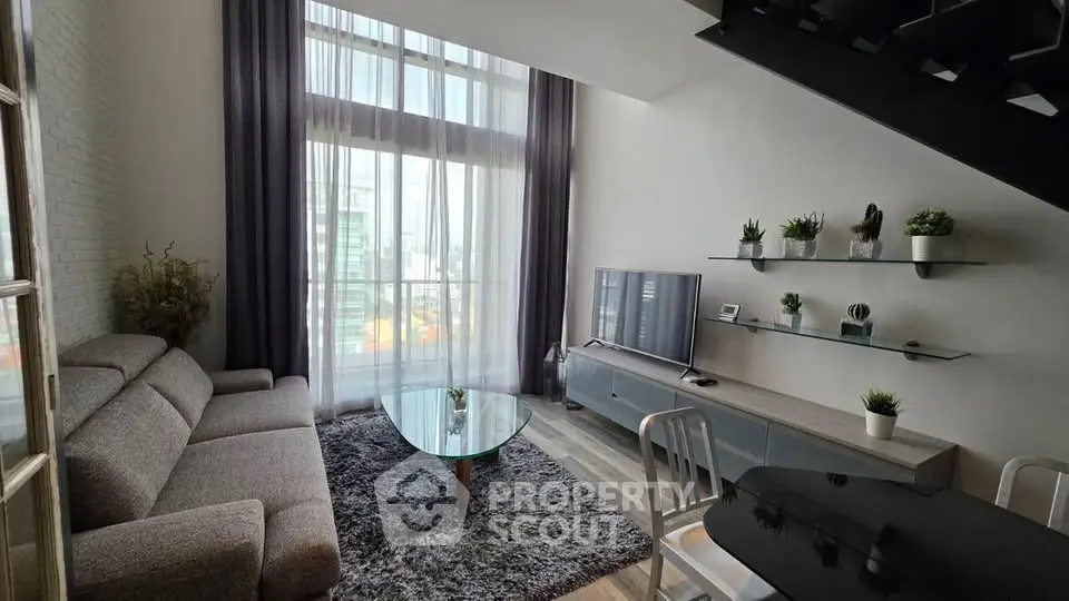 Modern living room with high ceilings, large windows, and stylish decor in urban apartment.