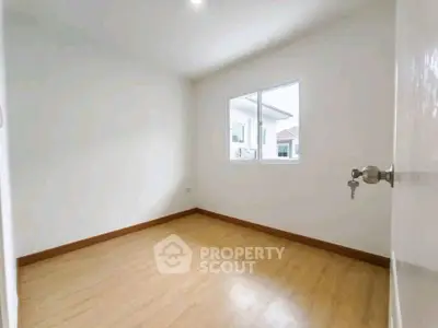 Spacious empty room with wooden flooring and bright window view.
