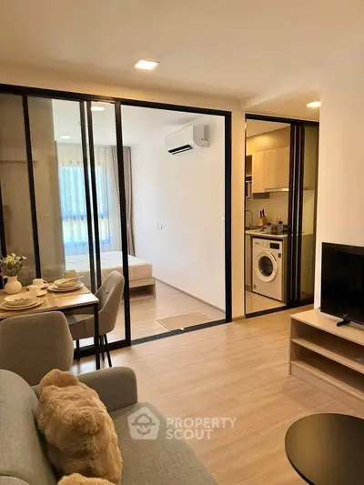 Modern open-plan living room with dining area and view into bedroom, featuring sleek furniture and natural light.