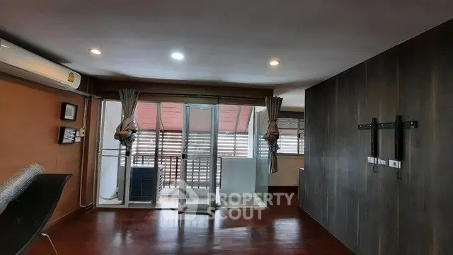 Spacious living room with sliding glass doors leading to a balcony, featuring modern lighting and wood flooring.