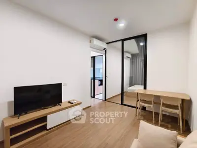 Modern living room with wooden flooring, TV unit, and glass partition leading to bedroom.