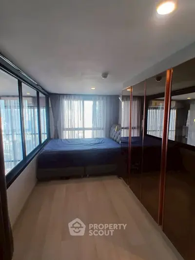 Spacious bedroom with large windows and mirrored closet doors, offering ample natural light.