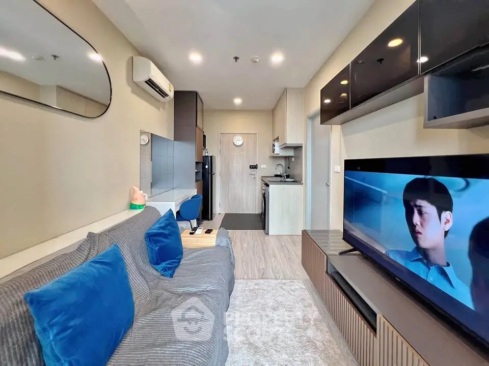 Modern living room with sleek design, featuring a cozy sofa, wall-mounted TV, and compact kitchen area.