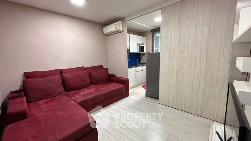 Modern living room with red sofa and compact kitchen in open layout apartment.