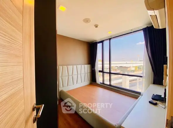 Modern bedroom with large window and wooden flooring, offering city views.