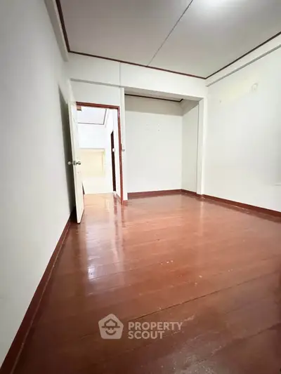 Spacious empty room with wooden flooring and white walls, ideal for customization.