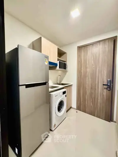 Modern kitchen with washing machine, fridge, and microwave in compact layout.