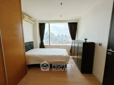 Modern bedroom with city view, featuring sleek furniture and large window for natural light.