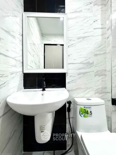 Modern bathroom with sleek white sink and toilet, featuring elegant black and white tile design.