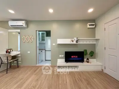 Modern living room with wooden flooring, TV setup, and open kitchen view.